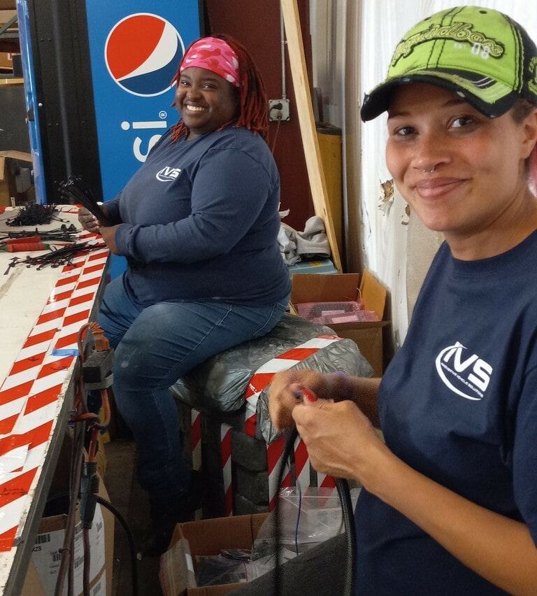 Two IVS workers sitting at a table with electrical cables smiling towards the camera.